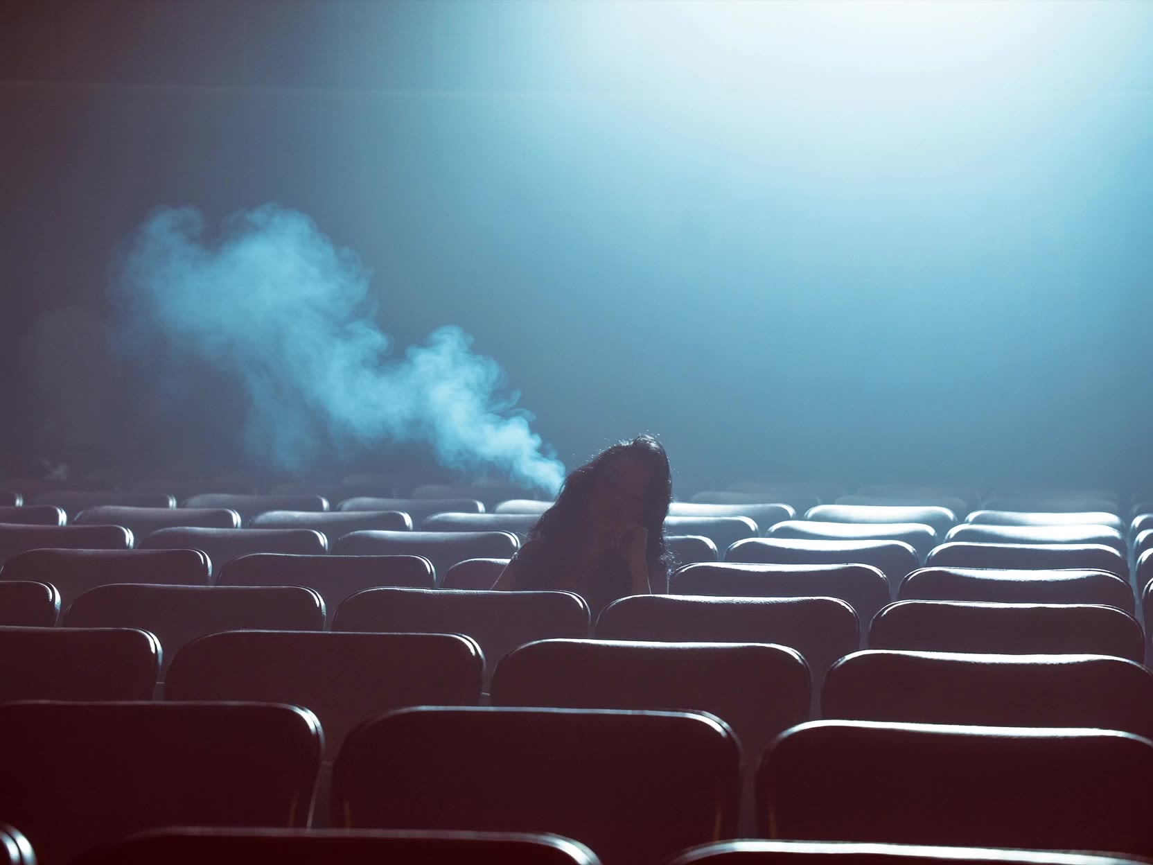 Lone figure in empty theater seats under volumetric blue light — LUCID DREAM set