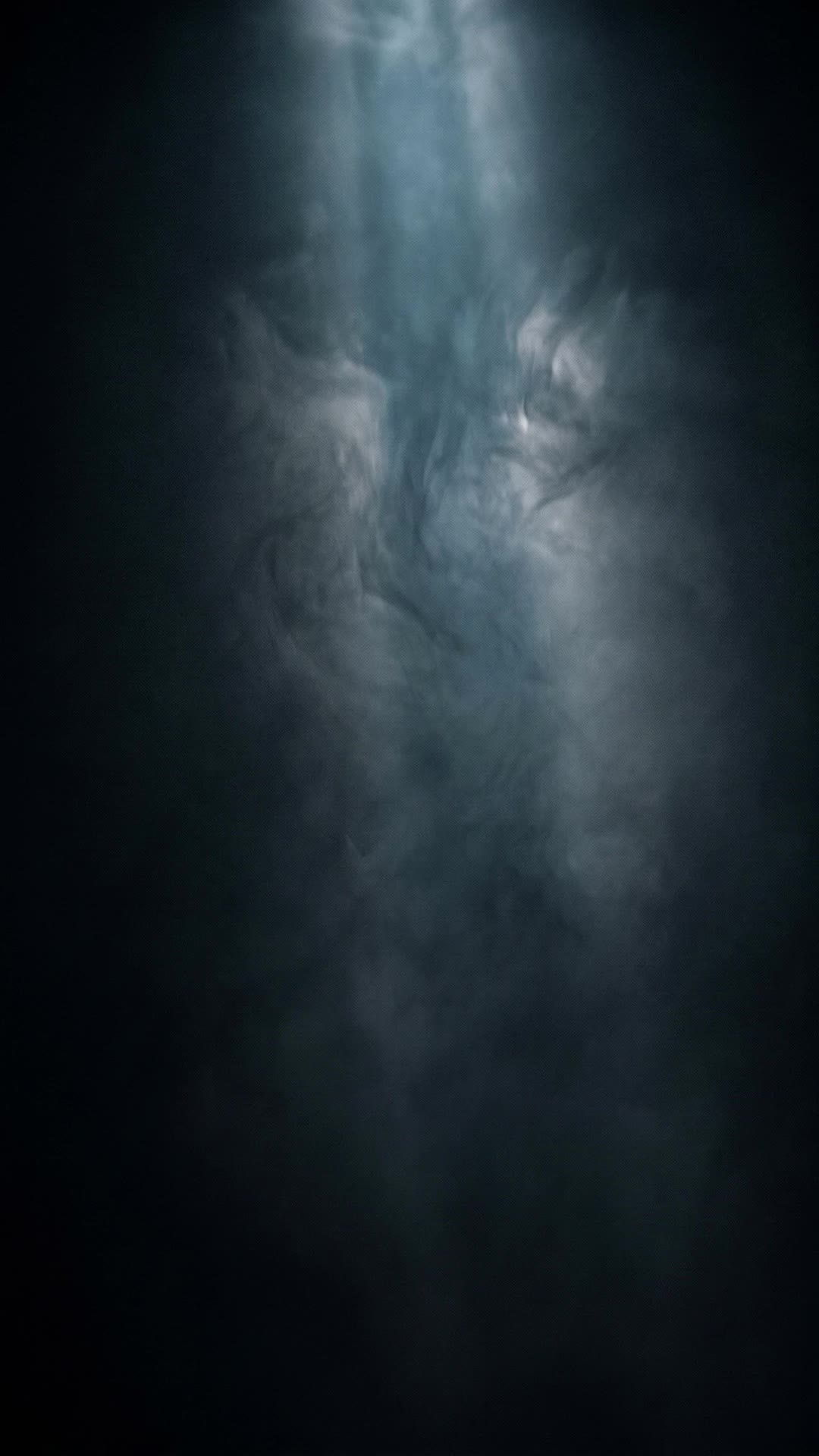 Slow volumetric haze drifting through a single faint steel-blue light shaft in near-black darkness