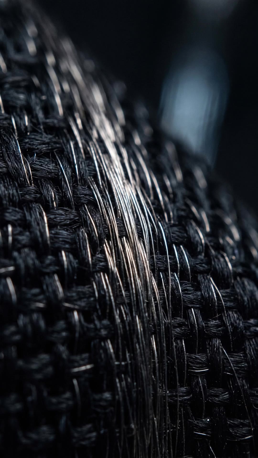 Macro of dark woven threads interlaced with brushed-metal filaments, a slow raking silver light